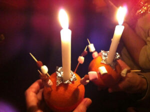 Christingle orange with lit candle and sweets on sticks